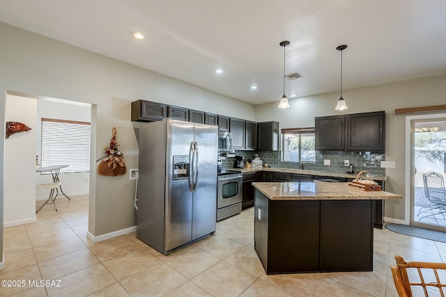 kitchen featuring tasteful backsplash, light stone counters, stainless steel appliances, decorative light fixtures, and a kitchen island