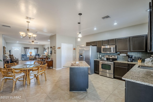 kitchen featuring light stone counters, ceiling fan with notable chandelier, decorative light fixtures, and appliances with stainless steel finishes