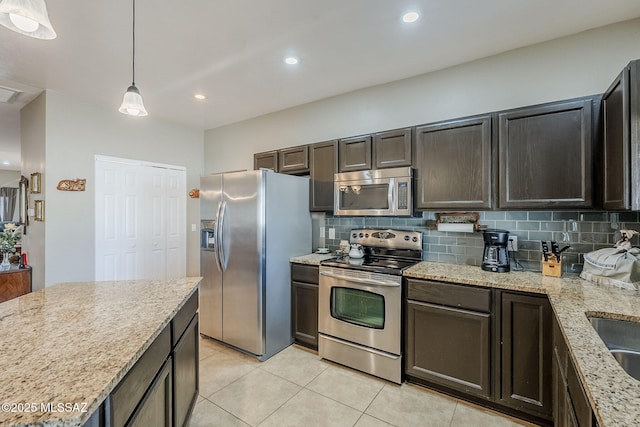 kitchen featuring pendant lighting, backsplash, appliances with stainless steel finishes, light stone counters, and dark brown cabinetry