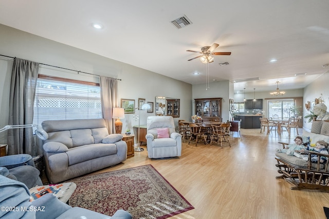 living room with ceiling fan with notable chandelier and light wood-type flooring