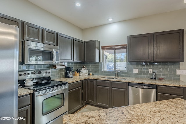 kitchen featuring sink, light stone countertops, appliances with stainless steel finishes, tasteful backsplash, and dark brown cabinets