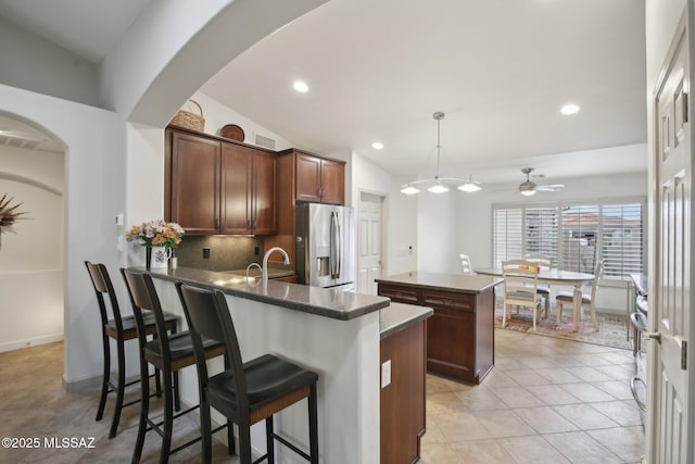 kitchen featuring pendant lighting, lofted ceiling, stainless steel refrigerator with ice dispenser, backsplash, and kitchen peninsula