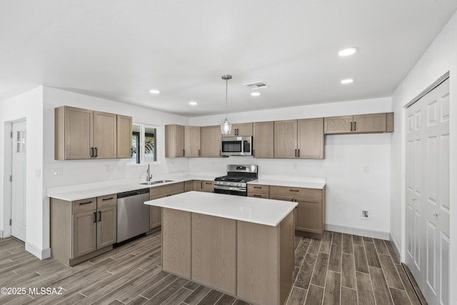 kitchen with sink, dark wood-type flooring, stainless steel appliances, decorative light fixtures, and a kitchen island