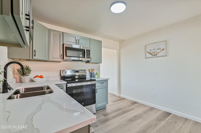 kitchen with light stone countertops, stainless steel appliances, light hardwood / wood-style floors, and sink