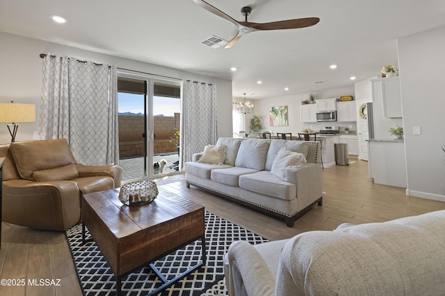 living room featuring ceiling fan with notable chandelier and light hardwood / wood-style flooring