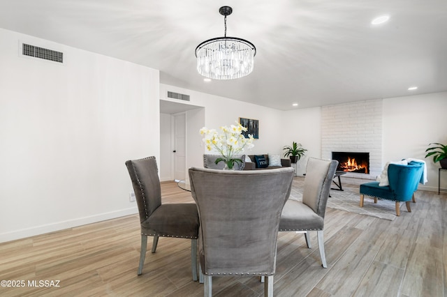 dining area featuring light hardwood / wood-style flooring, a chandelier, and a brick fireplace