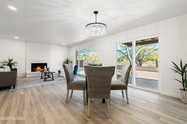 dining space with a chandelier, light wood-type flooring, and a brick fireplace