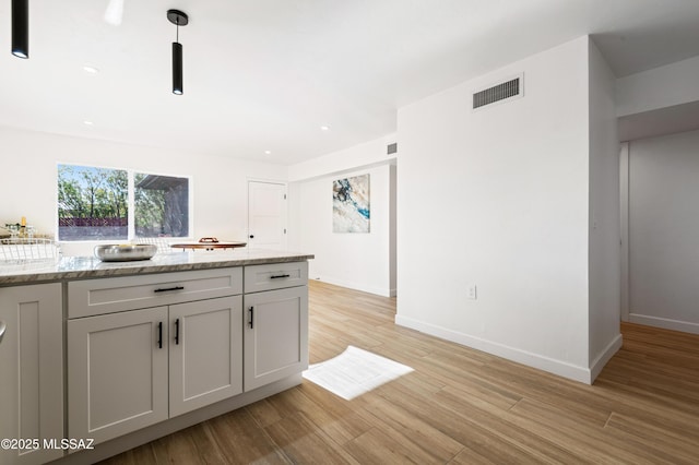 kitchen featuring pendant lighting, light hardwood / wood-style floors, and light stone counters