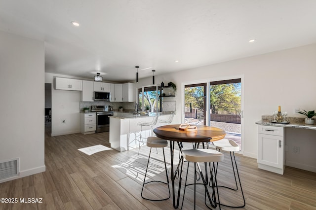 kitchen with white cabinets, hanging light fixtures, light hardwood / wood-style flooring, light stone counters, and stainless steel appliances