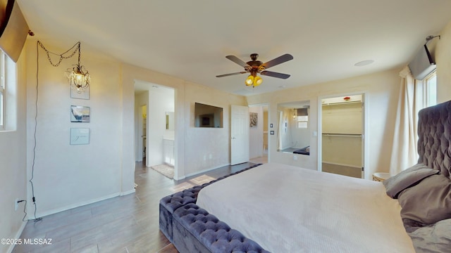 bedroom with a spacious closet, a closet, ceiling fan with notable chandelier, and light hardwood / wood-style flooring