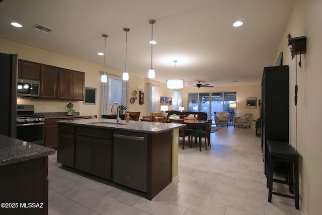 kitchen featuring sink, stainless steel appliances, dark stone countertops, an island with sink, and dark brown cabinets