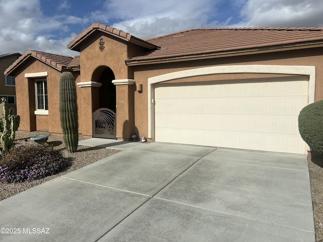 mediterranean / spanish-style house with a gate, driveway, an attached garage, stucco siding, and a tile roof