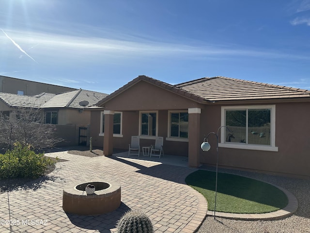 back of house with stucco siding, a tiled roof, a patio area, and an outdoor fire pit