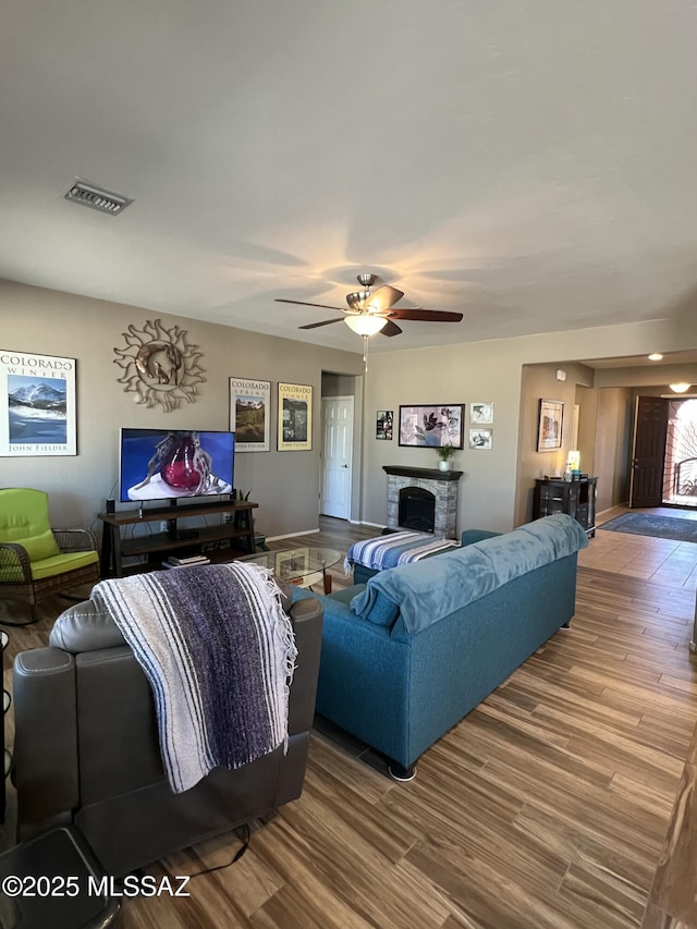 living area featuring visible vents, a stone fireplace, wood finished floors, and a ceiling fan