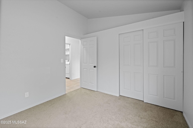 unfurnished bedroom featuring washer / clothes dryer, a closet, light colored carpet, and lofted ceiling