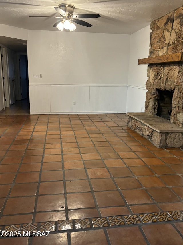 unfurnished living room with a textured ceiling, a fireplace, dark tile patterned floors, and ceiling fan