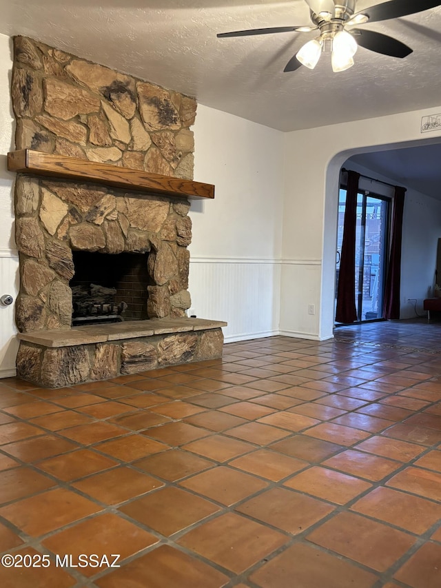 unfurnished living room featuring ceiling fan, a fireplace, tile patterned flooring, and a textured ceiling