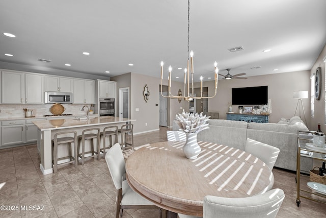 dining space with light tile patterned floors, ceiling fan with notable chandelier, and sink