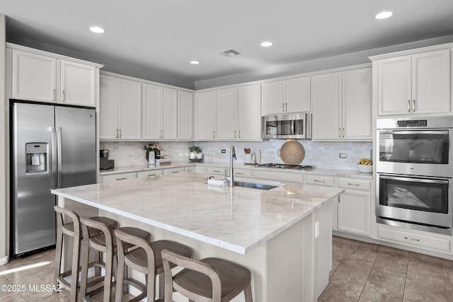 kitchen with white cabinets, appliances with stainless steel finishes, sink, and an island with sink