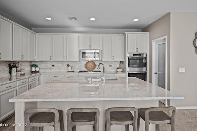 kitchen featuring a breakfast bar area, light stone countertops, an island with sink, and appliances with stainless steel finishes