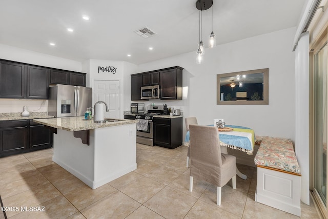 kitchen featuring a center island with sink, sink, hanging light fixtures, light stone countertops, and appliances with stainless steel finishes