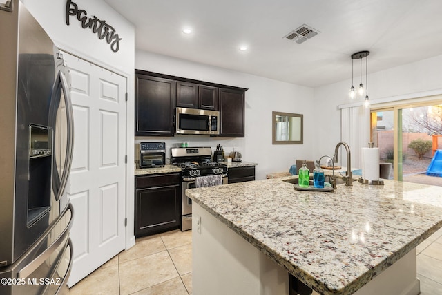 kitchen featuring decorative light fixtures, light stone countertops, stainless steel appliances, and a kitchen island with sink