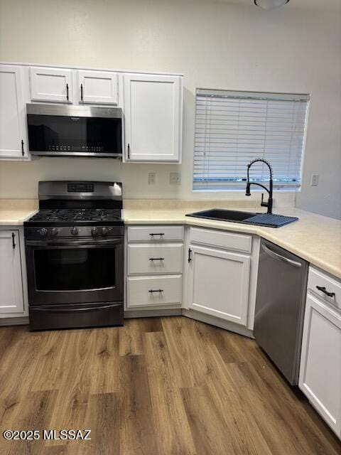 kitchen with sink, white cabinets, stainless steel appliances, and hardwood / wood-style flooring