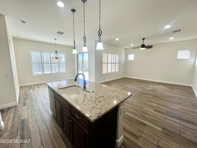 kitchen featuring a kitchen island with sink, hanging light fixtures, light stone countertops, plenty of natural light, and sink