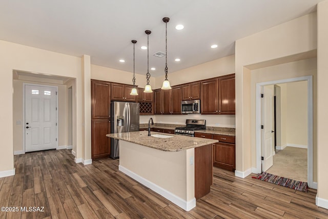 kitchen with sink, pendant lighting, dark hardwood / wood-style floors, stainless steel appliances, and an island with sink