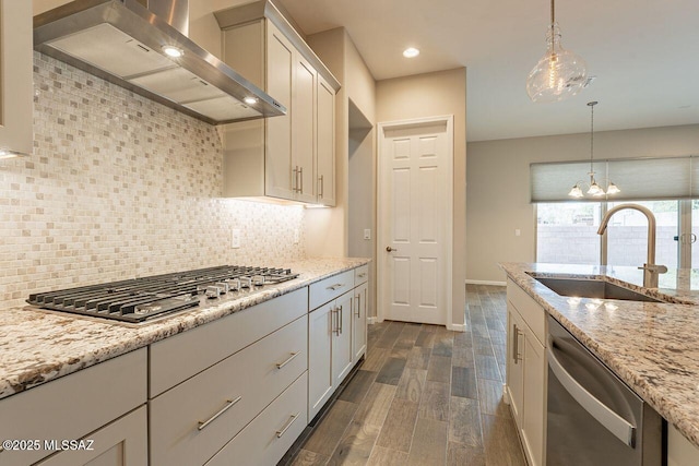 kitchen with light stone countertops, wall chimney exhaust hood, stainless steel appliances, decorative backsplash, and sink