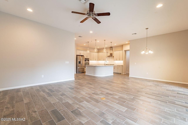 unfurnished living room featuring light wood-type flooring, ceiling fan with notable chandelier, and sink