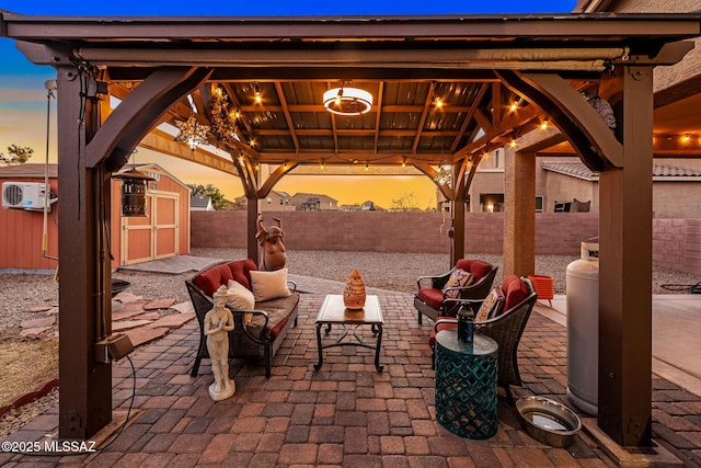 patio terrace at dusk with a gazebo, a storage unit, a wall mounted air conditioner, and outdoor lounge area