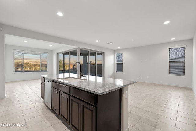 kitchen with dark brown cabinetry, light stone countertops, sink, a kitchen island with sink, and light tile patterned floors