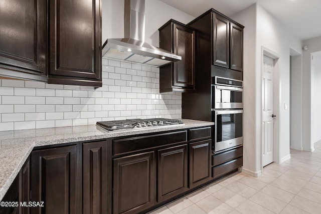 kitchen with wall chimney exhaust hood, light tile patterned floors, dark brown cabinetry, and appliances with stainless steel finishes