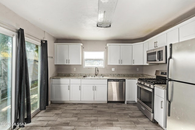 kitchen featuring appliances with stainless steel finishes, white cabinetry, a wealth of natural light, and sink