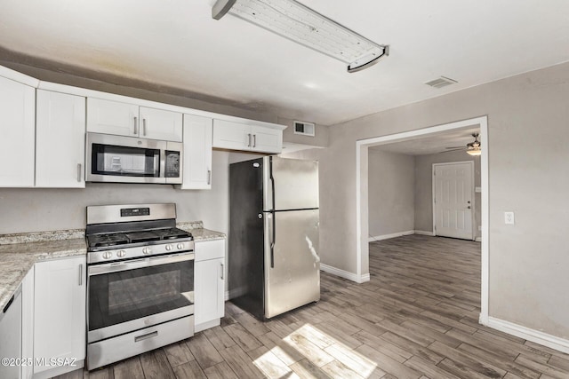 kitchen with hardwood / wood-style floors, light stone counters, white cabinetry, and appliances with stainless steel finishes