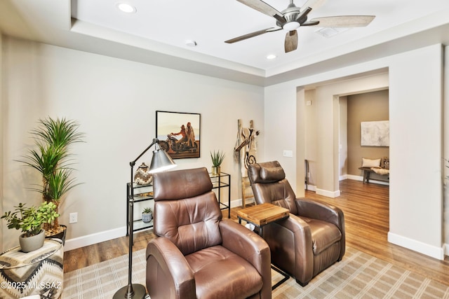 living area with a tray ceiling, ceiling fan, and wood-type flooring