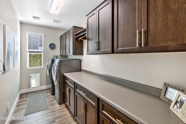 clothes washing area featuring cabinets, light hardwood / wood-style flooring, and washing machine and clothes dryer