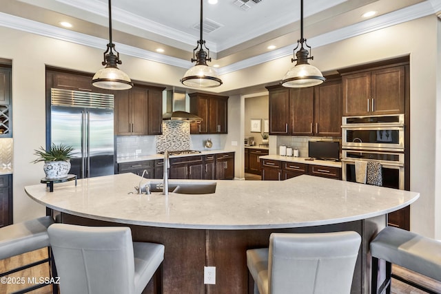 kitchen featuring pendant lighting, sink, appliances with stainless steel finishes, and wall chimney range hood