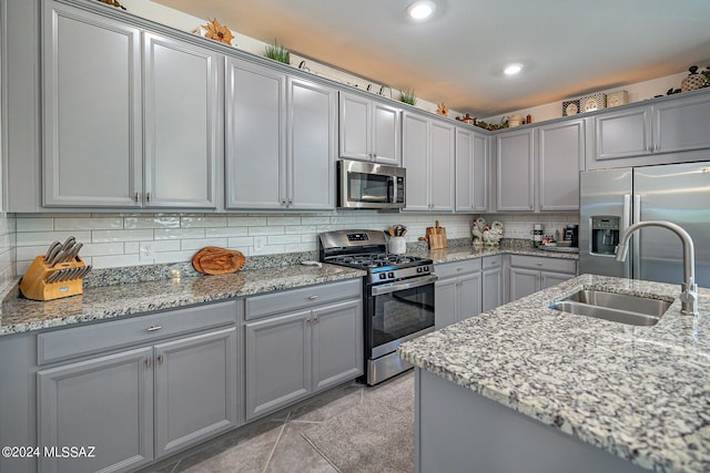 kitchen with light tile patterned floors, light stone countertops, sink, and appliances with stainless steel finishes