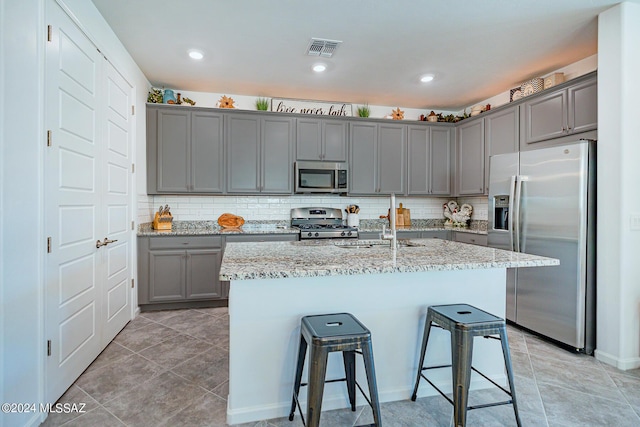 kitchen featuring a kitchen bar, light stone countertops, a kitchen island with sink, and appliances with stainless steel finishes