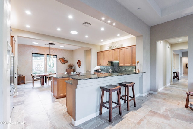 kitchen featuring kitchen peninsula, tasteful backsplash, dark stone counters, pendant lighting, and a kitchen island