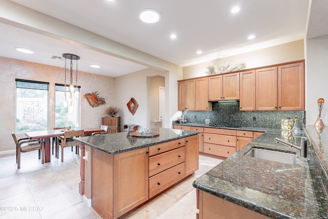 kitchen featuring sink, a center island, hanging light fixtures, and dark stone countertops