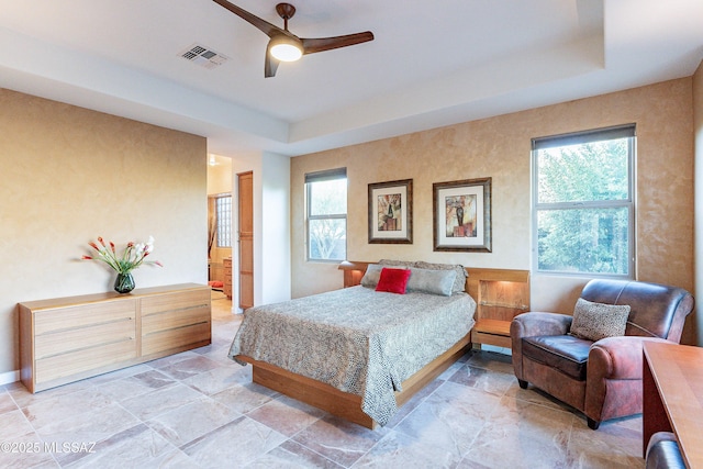 bedroom featuring ceiling fan, connected bathroom, and a tray ceiling