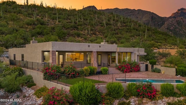 back house at dusk featuring a mountain view, a patio area, and a fenced in pool