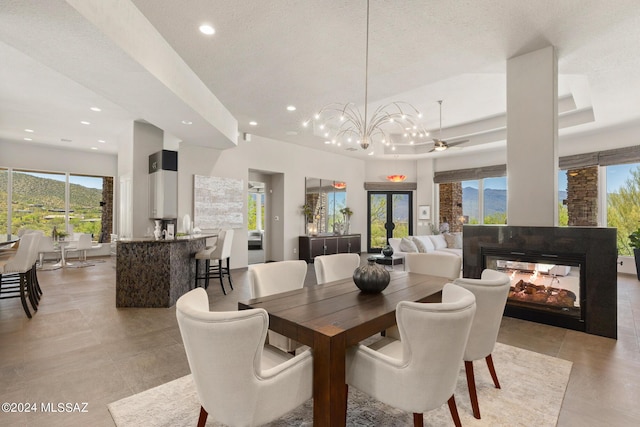 dining space featuring ceiling fan, a multi sided fireplace, plenty of natural light, and a tray ceiling