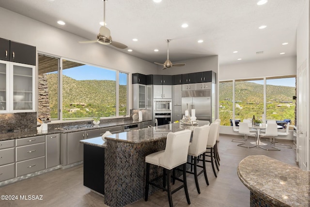 kitchen with ceiling fan, built in appliances, a mountain view, dark stone countertops, and a kitchen island