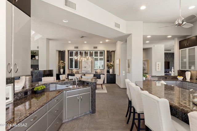 kitchen with gray cabinetry, dark stone counters, a kitchen breakfast bar, hanging light fixtures, and ceiling fan