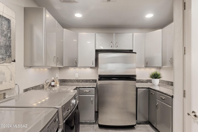 kitchen with white cabinets, washer / dryer, stainless steel refrigerator, and sink