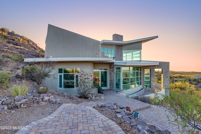 back house at dusk with a patio and a sunroom